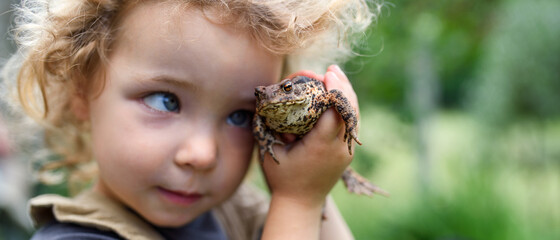 Close up portrait of small girl holding a frog outdoors in summer.
