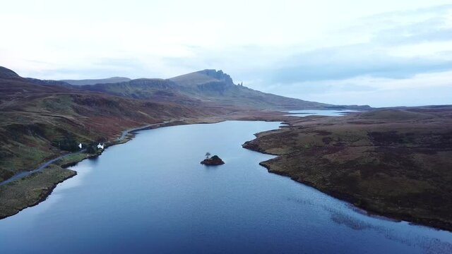 4k aerial footage of Loch Fada on the Isle of Skye looking towards the Old Man of Storr. Blue tones on calm water, early morning light.