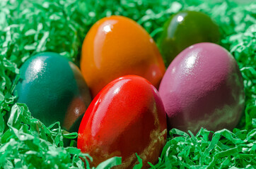 Fototapeta na wymiar Easter nest with multicolored Paschal eggs. Easter eggs arranged in a nest, made of green shredded paper. Group of hard boiled and colorful dyed chicken eggs, ready for a traditional egg hunt. Photo.