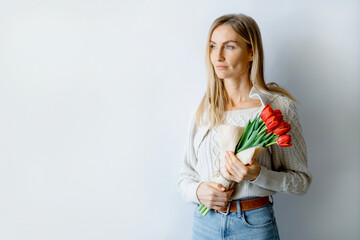 Young charming woman stands by the wall with a bouquet of tulips