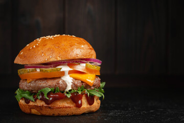 Delicious burger with beef and cheddar cheese on a dark wooden background. Tasty fresh unhealthy burgers with cheese and two patties. Fast food, unhealthy food concept.
