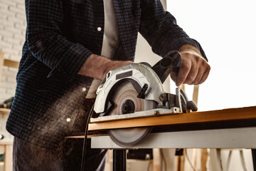 Carpenter hands cutting wood with electrical saw