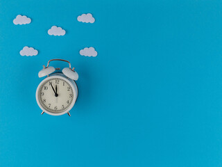 Alarm clock in the clouds on a blue background, shows about twelve o'clock. Time: 11.55 am or 23.55...