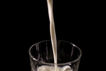 pouring milk in a glass. splash of white liquid isolated on dark background