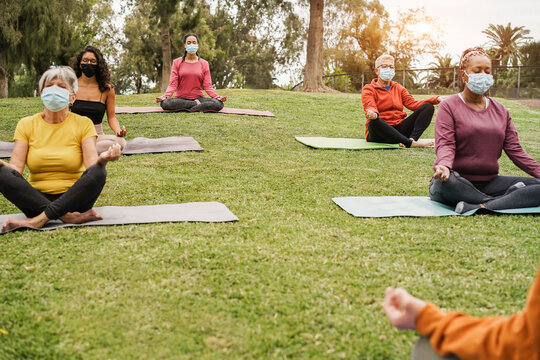 People doing yoga class outdoor sitting on grass while wearing safesty masks during coronavirus outbreak - Social distance and sport concept - Main focus on bottom girl face - Powered by Adobe