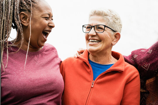 Happy senior women from different ethnicities laughing together outdoor - Multiracial mature friends having fun - Joyful elderly lifestyle - Focus on right female face