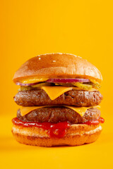 Delicious burger with double beef and cheddar cheese on a yellow background. Tasty fresh unhealthy burgers with cheese and two patties. Fast food, unhealthy food concept.