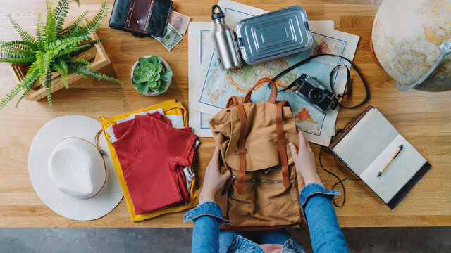 Top view of young woman packing for vacation trip holiday, desktop travel concept.
