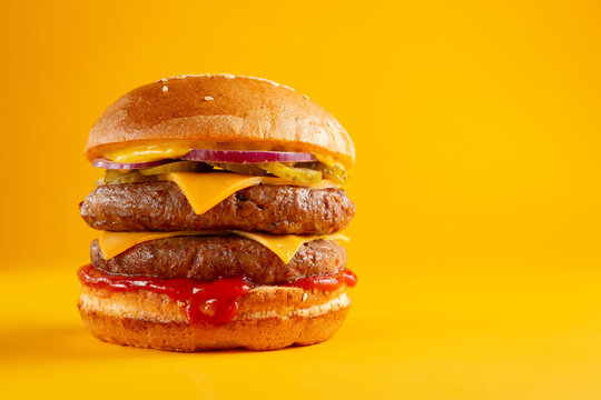 Delicious burger with double beef and cheddar cheese on a yellow background. Tasty fresh unhealthy burgers with cheese and two patties. Fast food, unhealthy food concept.