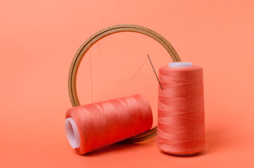 Closeup of spools of orange threads, embroidery hoops on the orange background