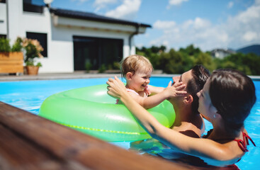 Fototapeta na wymiar Young family with small daughter in swimming pool outdoors in backyard garden.