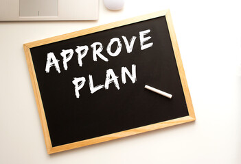 Text APPROVE PLAN written in chalk on a slate board. Office desk.