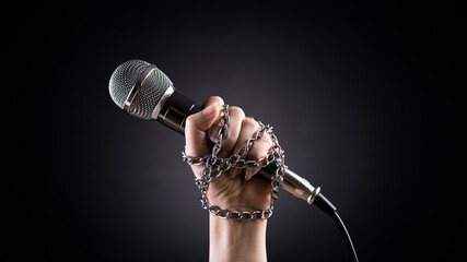 World press freedom day concept. Hand holding a microphone with chain on dark background, symbol of...