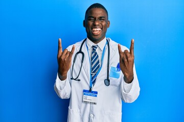 Young african american man wearing doctor uniform shouting with crazy expression doing rock symbol with hands up. music star. heavy concept.