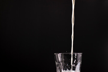 pouring milk in a glass. splash of white liquid isolated on dark background