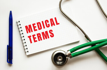 MEDICAL TERMS is written in a notebook on a white table next to pen and a stethoscope.
