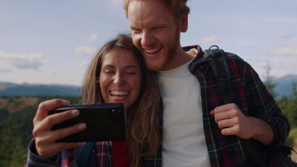 Couple watching funny video on mobile phone. Hikers using cellphone during hike 