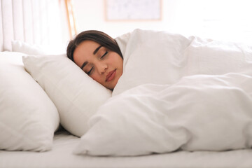 Fototapeta na wymiar Young woman covered with warm white blanket sleeping in bed at home