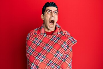 Handsome hispanic man wrapped in a red warm red blanket angry and mad screaming frustrated and furious, shouting with anger looking up.