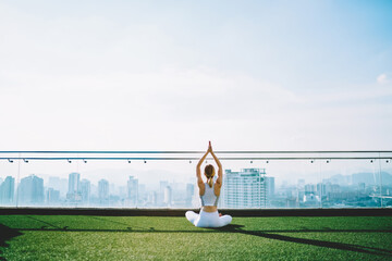 Woman doing yoga on roof of skyscraper in sunny morning
