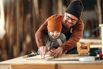 Happy family father and son working together in carpentry workshop - obrazy, fototapety, plakaty