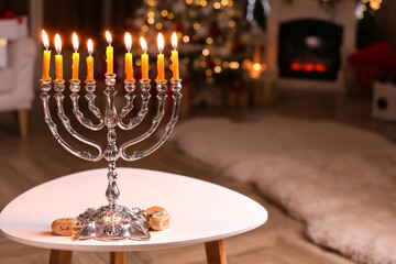 Silver menorah near dreidels with symbols He, Pe, Nun, Gimel on white table in room, space for text