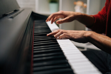 Obraz na płótnie Canvas Close-up hands of unrecognizable musician man playing on synthesize at home studio. Closeup view of pianist male playing on digital piano in living room. Concept of music education.