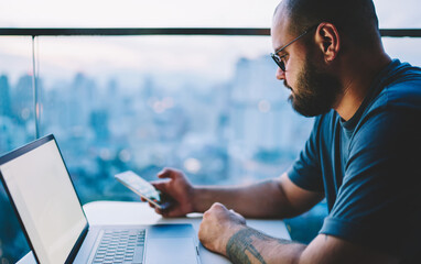 Serious man with laptop surfing smartphone