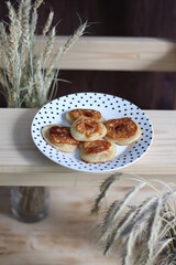 pancakes stuffed with apple jam on plate on wooden background with wheat spikes