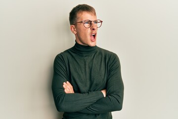 Young caucasian man wearing glasses with arms crossed gesture angry and mad screaming frustrated and furious, shouting with anger. rage and aggressive concept.