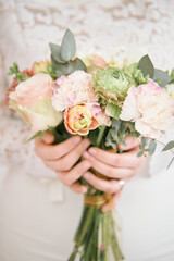 Wedding bouquet in the hands of the bride close-up. An original bouquet of different flowers - ranunculus, carnations, roses, eucalyptus. Blur and selective focus.