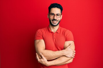 Fototapeta premium Young hispanic man wearing casual clothes and glasses happy face smiling with crossed arms looking at the camera. positive person.