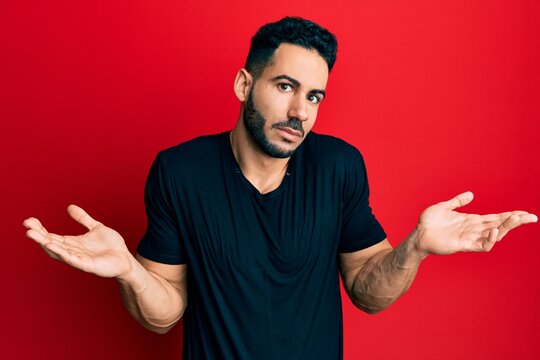 Young hispanic man wearing casual black t shirt clueless and confused with open arms, no idea and doubtful face.