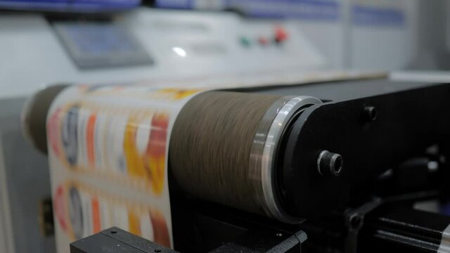 Conveyor of slitter rewinding inspection machine with fast moving printed labels at printer exhibition, trade show - close up. Technology, manufacturing, food packaging, advertising concept