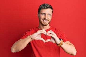 Handsome caucasian man wearing casual red tshirt smiling in love doing heart symbol shape with...