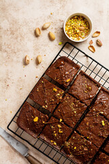 Chocolate squares with pistachio nuts and strawberries on a metal stand on a light stone background, top view, horizontal composition. Flat lay