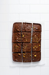 Chocolate squares with pistachio nuts and strawberries on white paper on a light background, top view, horizontal composition. Flat food