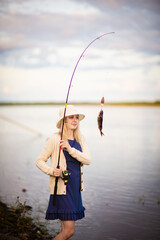 a girl fisherman in a blue dress and hat caught a perch, Selective focus