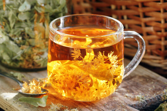 Linden herbal tea with flowers in a glass cup on wooden rustic board with lime blossom dry herb nearby, closeup, drink for relaxation, mental health,  naturopathy, homeopathy and folk medicine concept