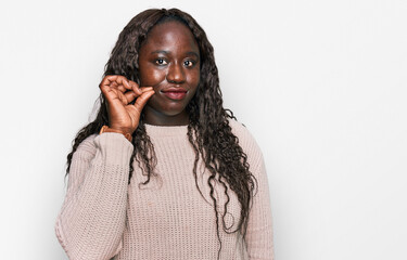 Young african woman wearing wool winter sweater mouth and lips shut as zip with fingers. secret and...
