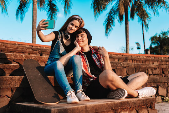 Young couple with skateboard taking selfie outdoors.