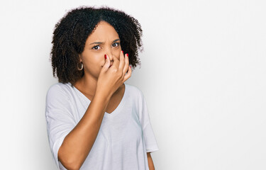 Young african american girl wearing casual clothes smelling something stinky and disgusting, intolerable smell, holding breath with fingers on nose. bad smell