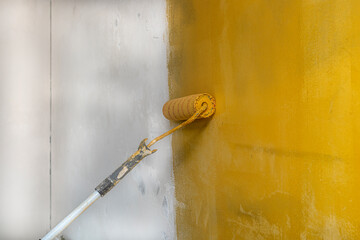 Process of applying yellow primer to the wall. Worker's hand with big roller