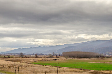 Obraz premium Bulgarian Countryside During Winter Season with Fields, Bare Trees, Cloudy Sky and Mountains in Background. South Bulgaria, Europe