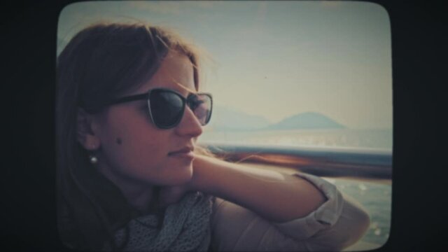 A young tourist woman with sunglasses riding on a boat, looking at the coastal landscapes. Vintage Film Look. 