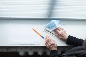 financial difficulties in the family. The impact of quarantine on the lives of the elderly. Reaping hands of a woman with a mask. Elderly hands are writing a will.