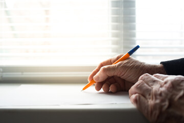 Elderly hands  writing with pen. Old hands writting a will. Old hands writting on windowsill.