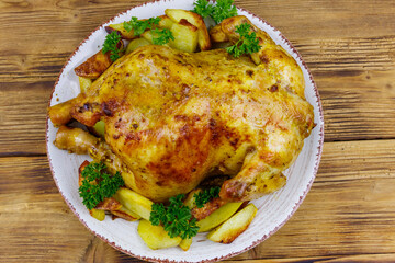 Baked whole chicken with potato on a wooden table. Top view