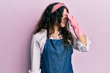 Young brunette woman with curly hair wearing cleaner apron and gloves tired rubbing nose and eyes feeling fatigue and headache. stress and frustration concept.