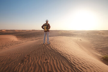 Fototapeta na wymiar Desert adventure. Young man with backpack walking on sand dune. Dubai, United Arab Emirates